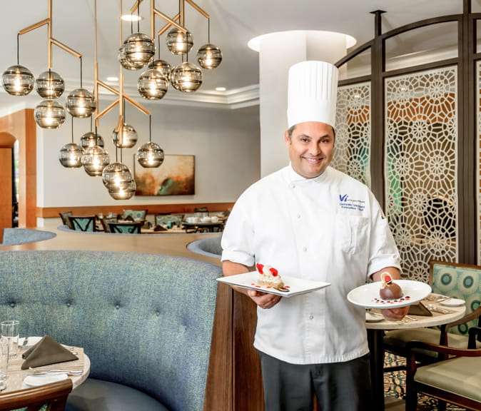 Vi's executive chef holds two dishes in the Arrosti dining room.