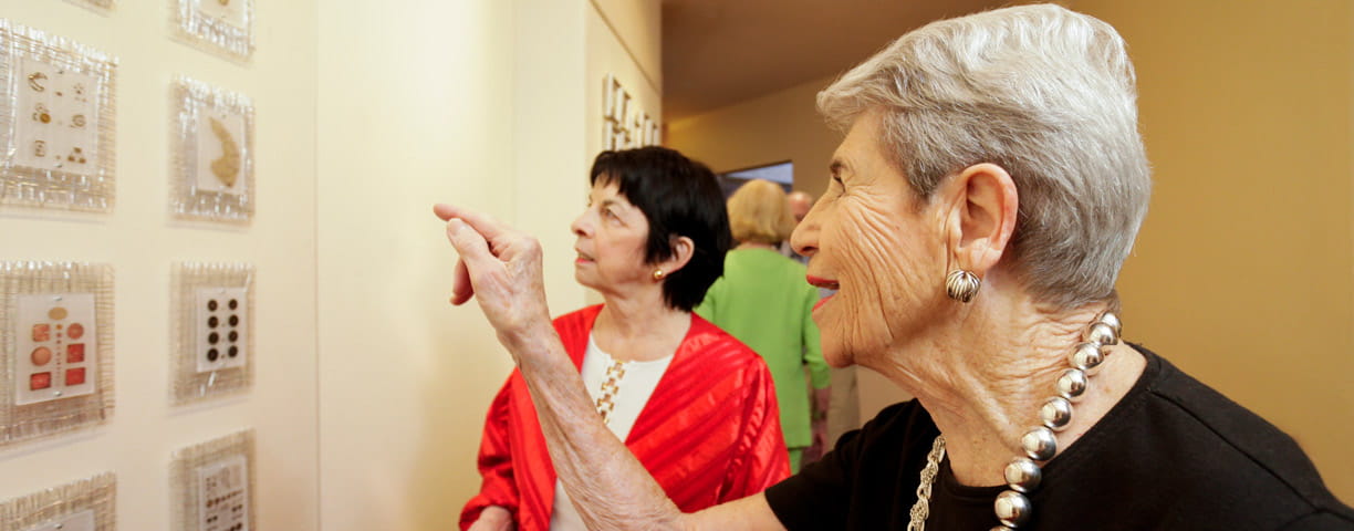 Two women admire art at a gallery event.